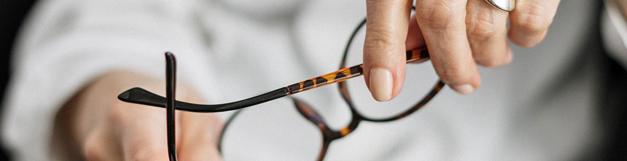 EineFrau mit einer weißen Bluse hält eine aufgeklappte Brille in den Händen